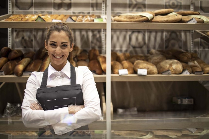 portrait-bakery-seller-with-arms-crossed-standing-front-shelf-full-bred-bagels-pastry.jpg