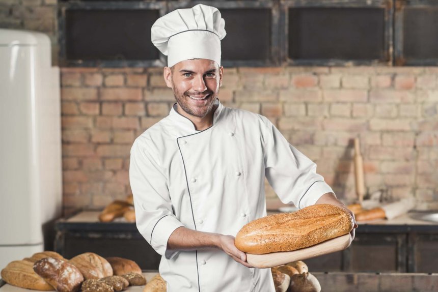 smiling-male-baker-holding-baked-bread-chopping-board_1.jpg