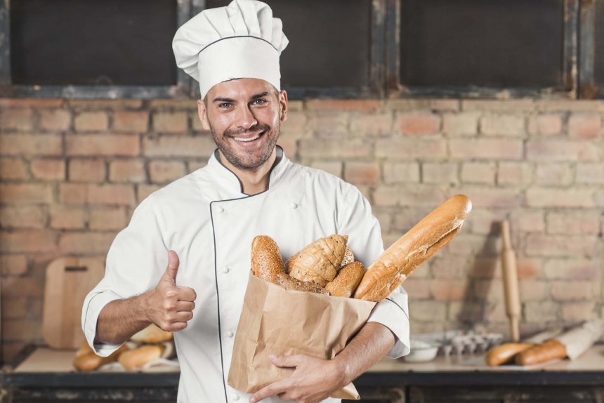 smiling-young-male-baker-holding-loaf-breads-paper-bag-showing-thumb-up-sign_1.jpg
